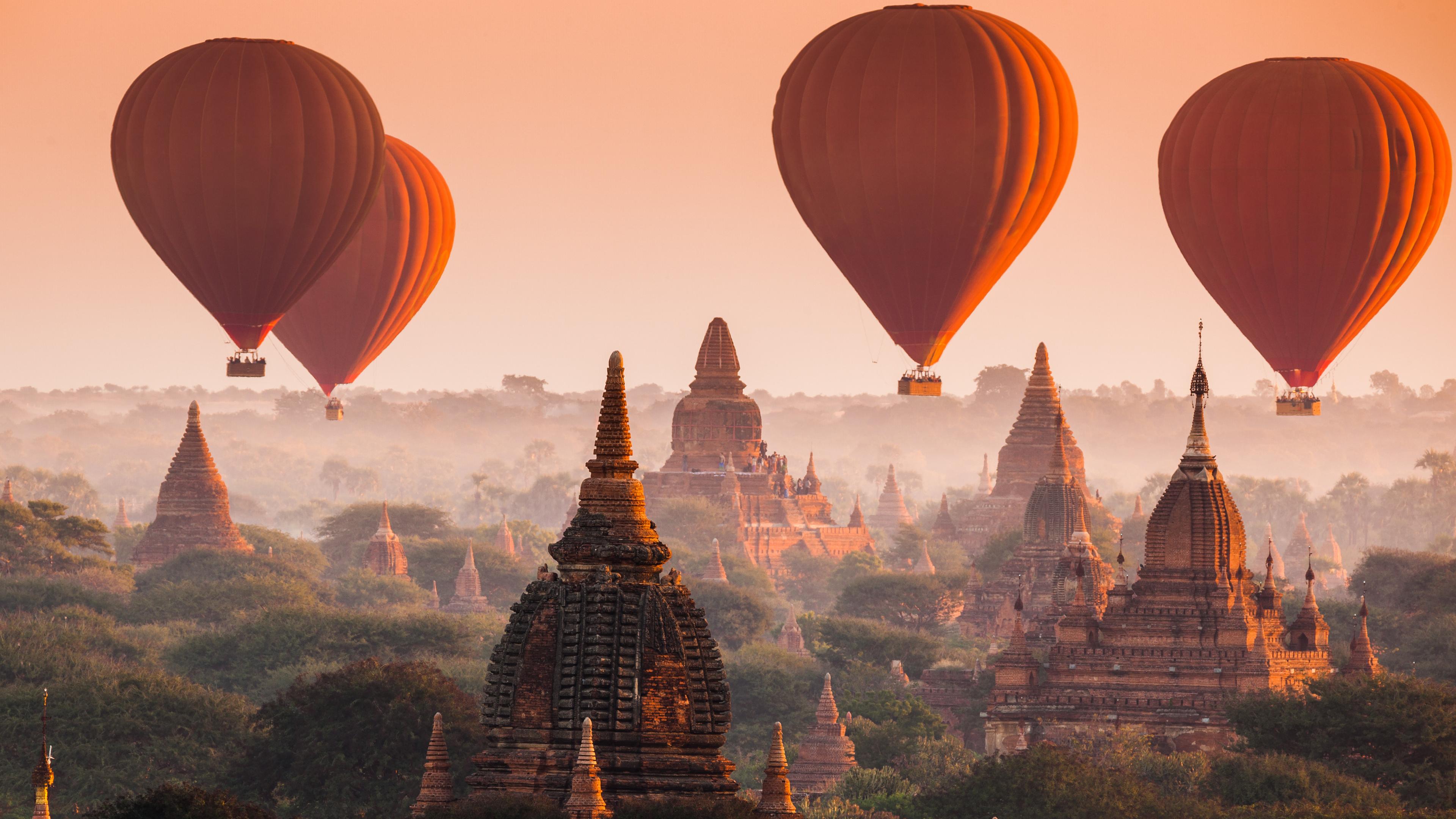 Heißluftballons schweben über Pagoden im Nebel.