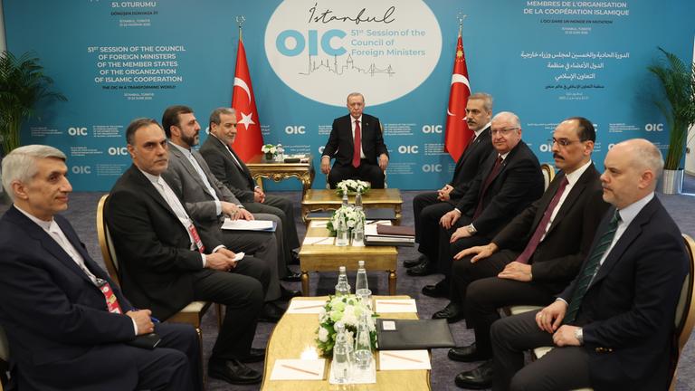 Ein Konfernzraum. Der türkische Präsident sitzt vor Kopf. Die anderen Staatsoberhäupter sitzen an der Seite in Anzügen. In der Mitte stehen mehrere kleine Tische.