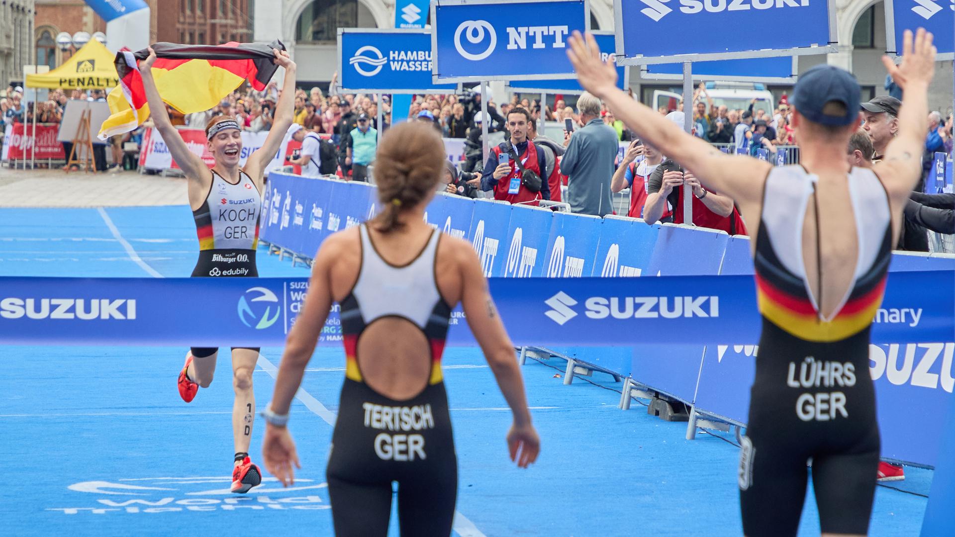Annika Koch hält beim Zieleinlauf eine Deutschlandfahne während Lisa Tertsch und Lasse Lührs hinter der Ziellinie auf sie warten.