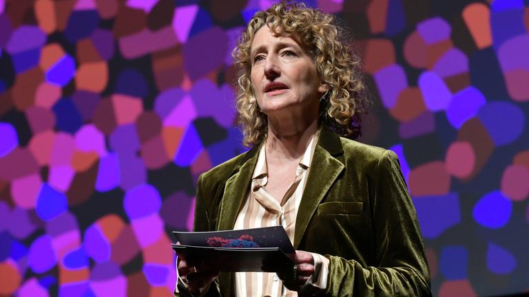 Frau spricht auf der Bühen und hält ein Manuskript in den Händen.