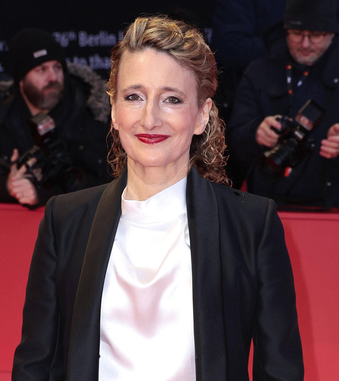 Frau steht auf rotem Teppich und schaut lächelnd in die Kamera.