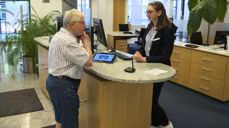 Roland in einer Bank am Schalter mit Bankangestellten