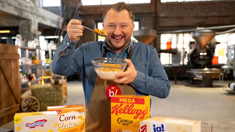 Sebastian Lege steht vor unterschiedlichen Packungen mit Cornflakes und lässt Flakes in eine Schüssel rieseln.