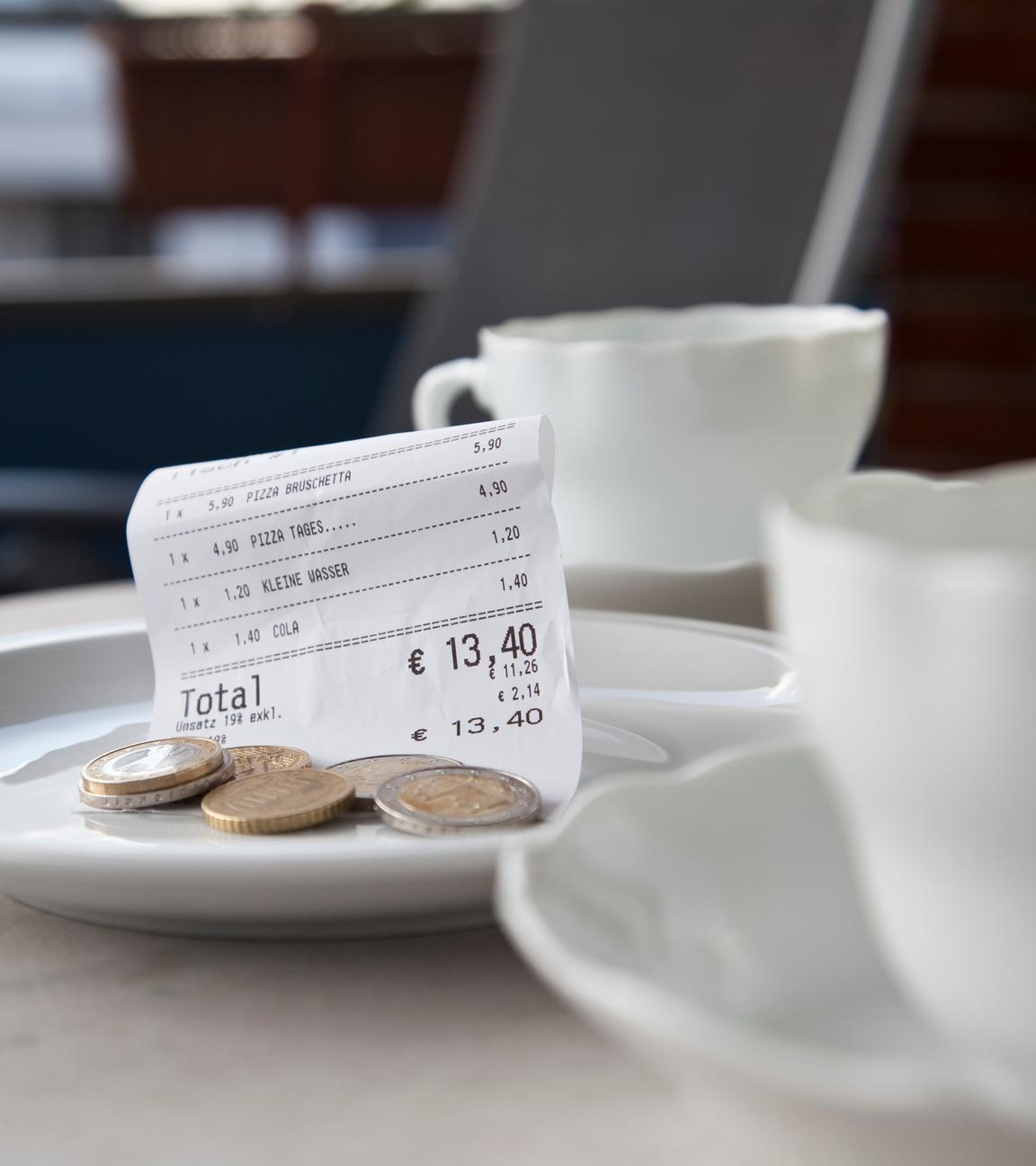 Zwei Kaffeetassen auf einem Restauranttisch, daneben ein Tellerchen mit einem Kassenbon und Münzen
