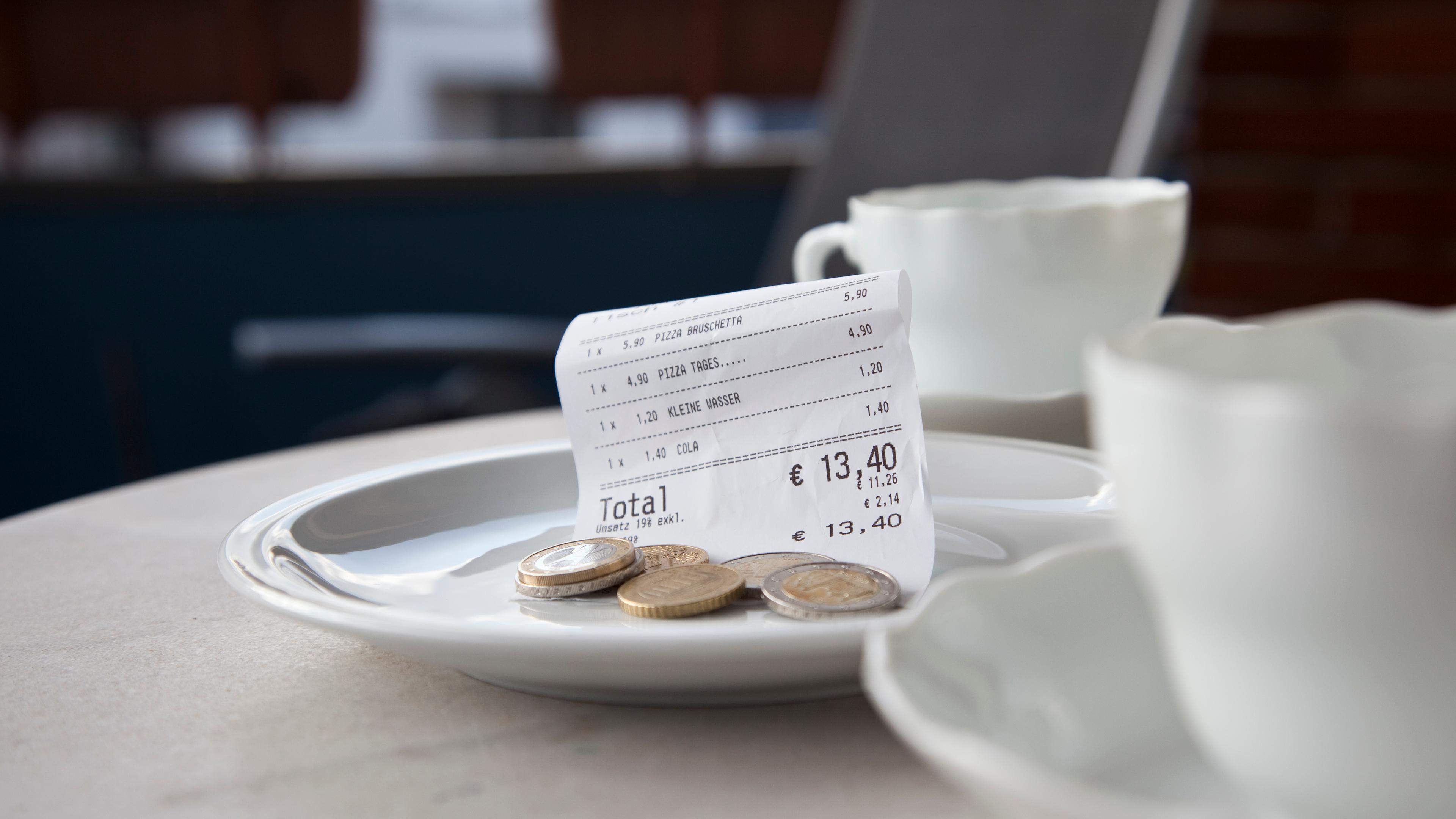 Zwei Kaffeetassen auf einem Restauranttisch, daneben ein Tellerchen mit einem Kassenbon und Münzen