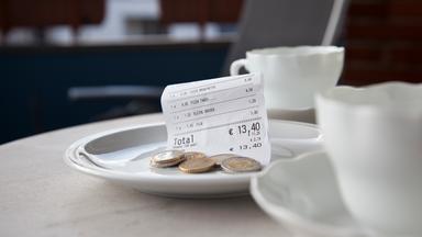 Zwei Kaffeetassen auf einem Restauranttisch, daneben ein Tellerchen mit einem Kassenbon und Münzen
