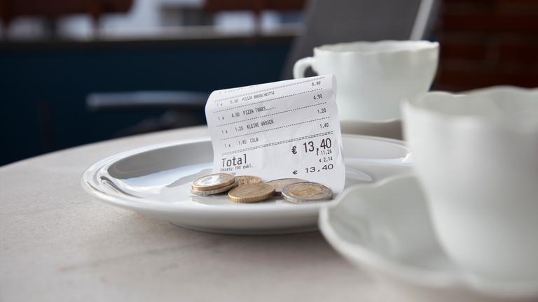 Zwei Kaffeetassen auf einem Restauranttisch, daneben ein Tellerchen mit einem Kassenbon und Münzen