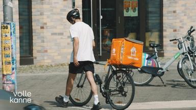 Ein Lieferando-Bote schiebt ein Fahrrad. 