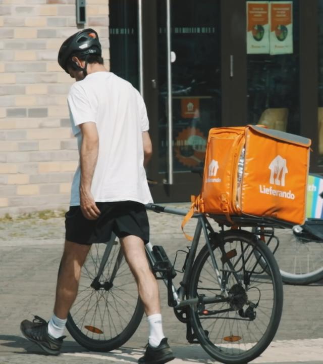 Ein Lieferando-Bote schiebt ein Fahrrad. 