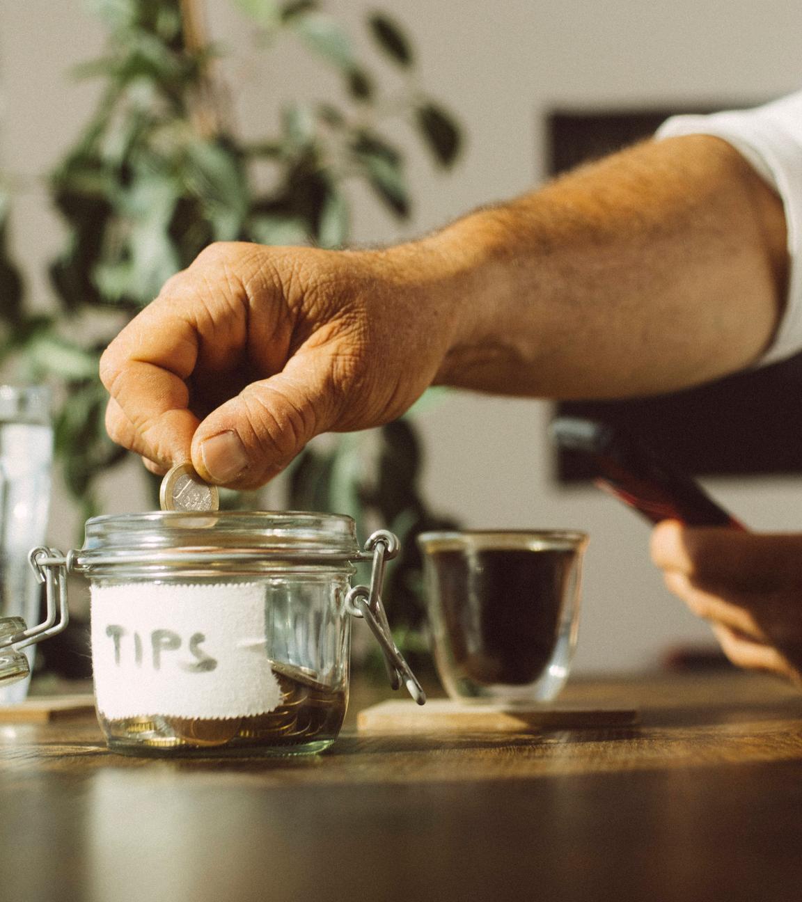 Mann wirft Münze in ein Trinkgeldglas in einem Café.