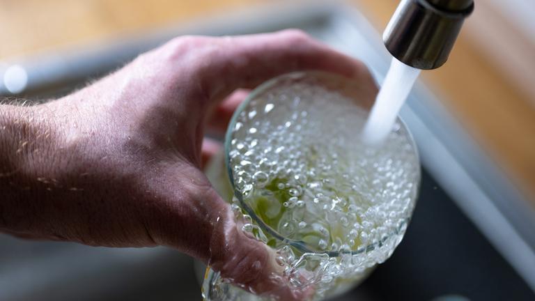 Trinkwasser läuft aus dem Wasserhahn in einer Küche in ein Glas mit Limettenstücken.