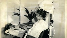 Woman under hairdryer at hairdresser writing on typewriter - 1959