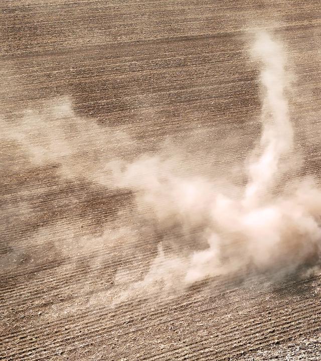 Ein Traktor zieht ein landwirtschaftliches Gerät über ein extrem trockenes Feld und wirbelt dabei eine riesige Staubwolke auf, aufgenommen am 14.08.2026