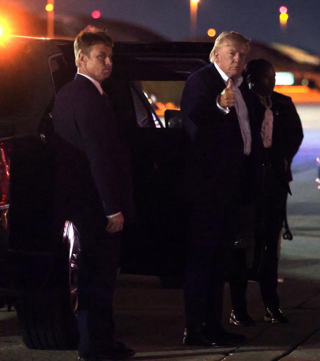 Donald Trump steht im Dunkeln auf einem Rollfeld und zeigt den Daumen hoch in Richtung Kamera.