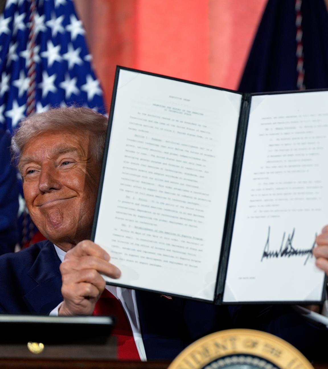 US-Präsident Trump hält das unterschriebene Papier mit der neuen KI-Strategie und grinst