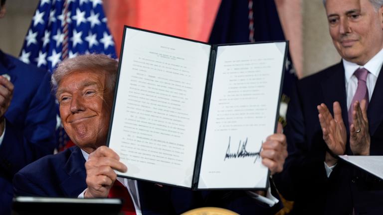 US-Präsident Trump hält das unterschriebene Papier mit der neuen KI-Strategie und grinst