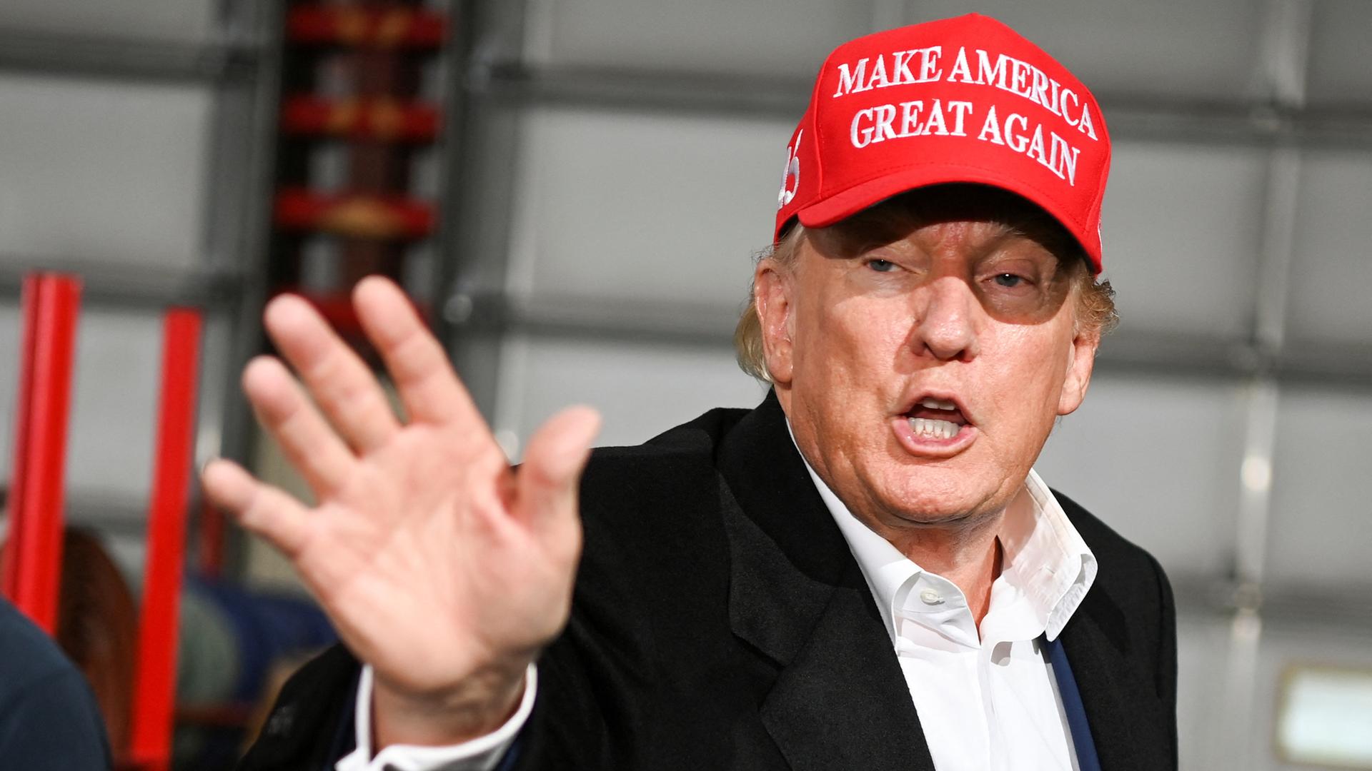 Donald Trump gestikuliert und trägt eine rote Schirmmütze. 