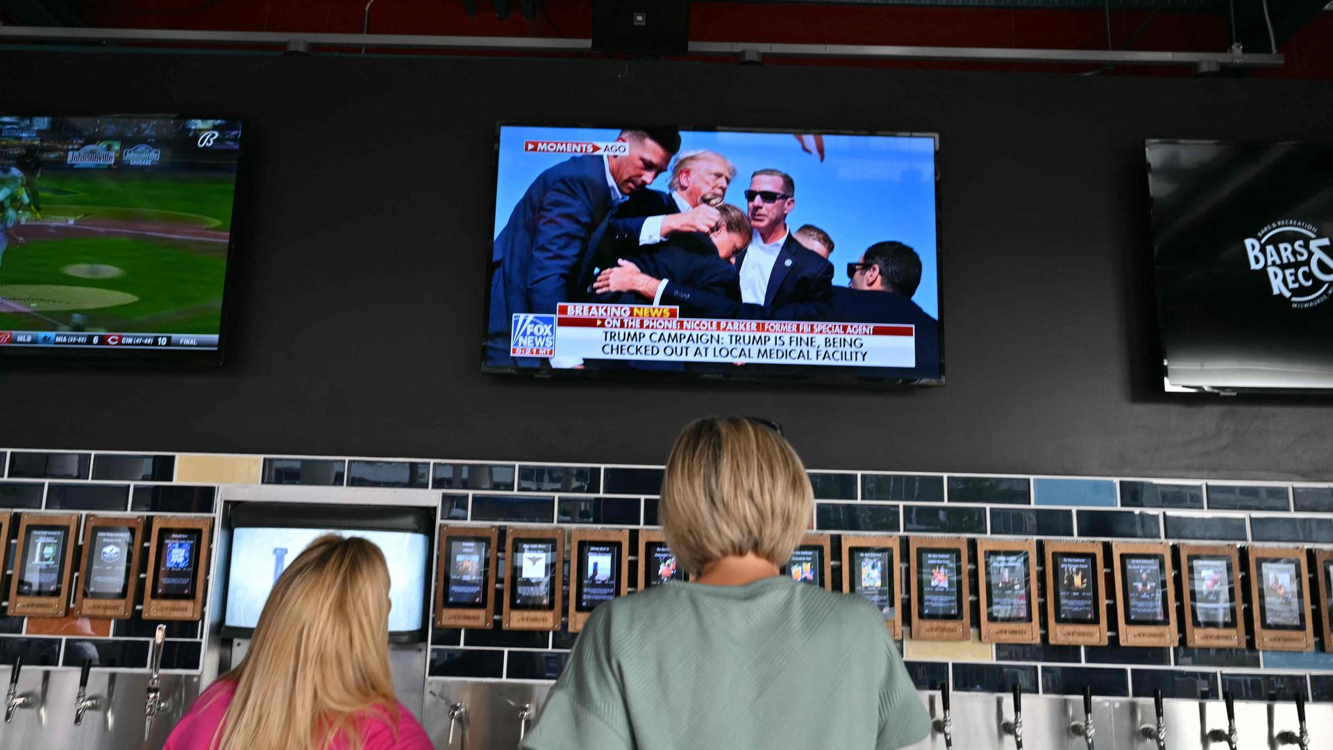 Menschen schauen die Nachrichten zum Trump-Attentat vor einem Fernseher.