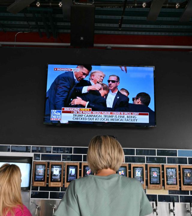 Menschen schauen die Nachrichten zum Trump-Attentat vor einem Fernseher.