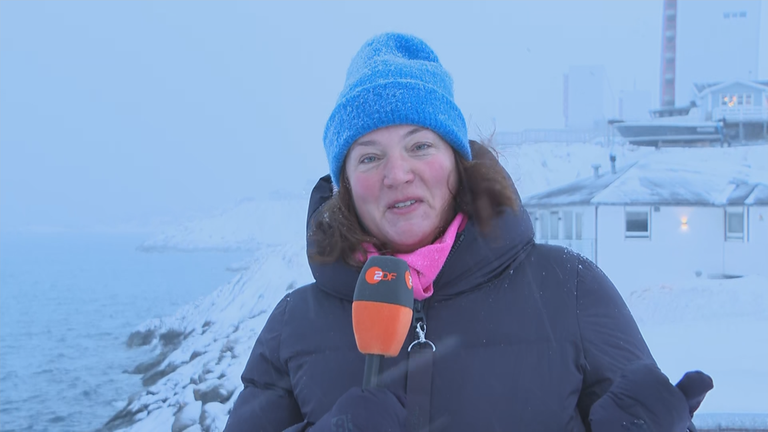 Winnie Heescher vor verschneiten Klippen und einem Gebäude auf Grönland.