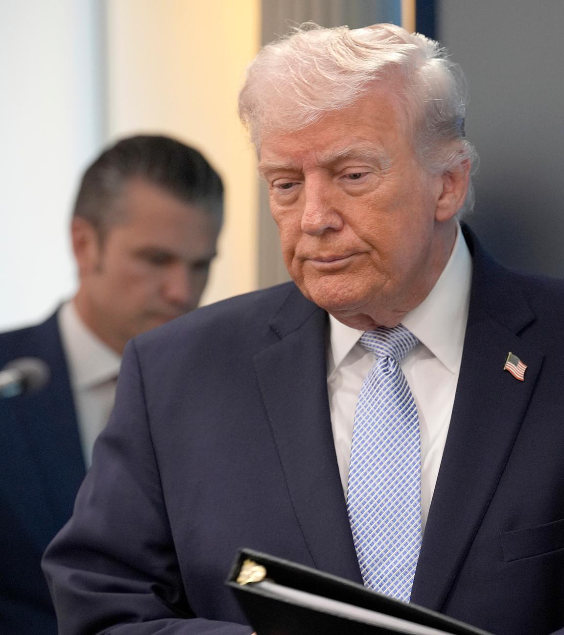US-Präsident Donald Trump im Presseraum des Weißen Hauses mit gesenktem Blick. Im Hintergrund steht Kriegsminister Hegseth.