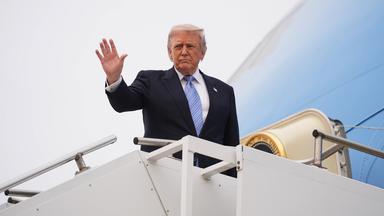 Trump steigt in ein Flugzeug und hebt die Hand
