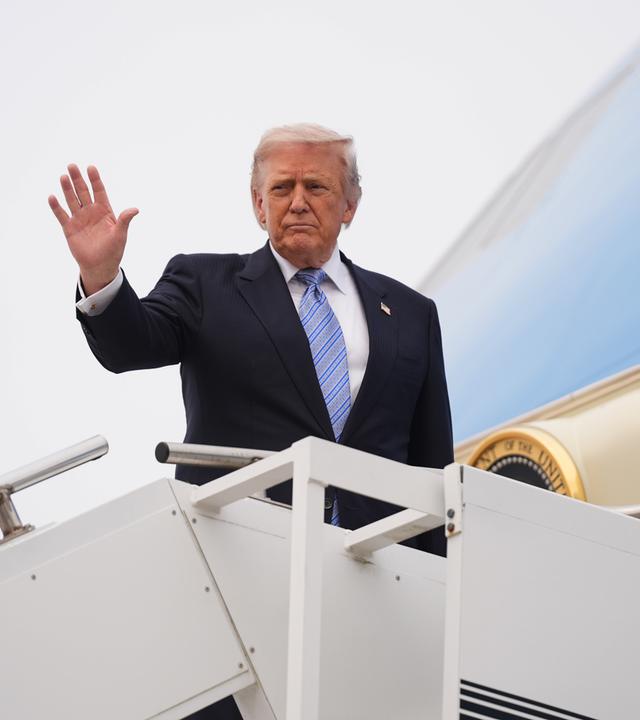 Trump steigt in ein Flugzeug und hebt die Hand