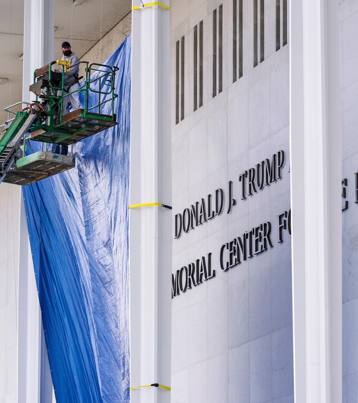 Bauarbeiter sind auf zwei grünen Hebebühnen an der Fassade des Kennedy Centers in Washington. Neben ihnen prangt der neue "Trump"-Schriftzug.