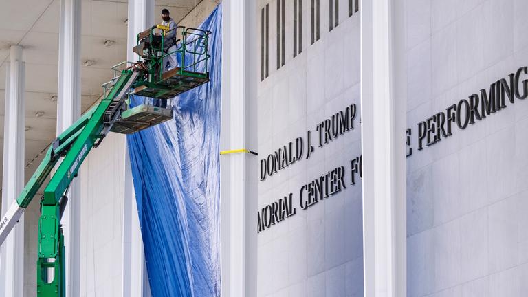 Bauarbeiter sind auf zwei grünen Hebebühnen an der Fassade des Kennedy Centers in Washington. Neben ihnen prangt der neue "Trump"-Schriftzug.