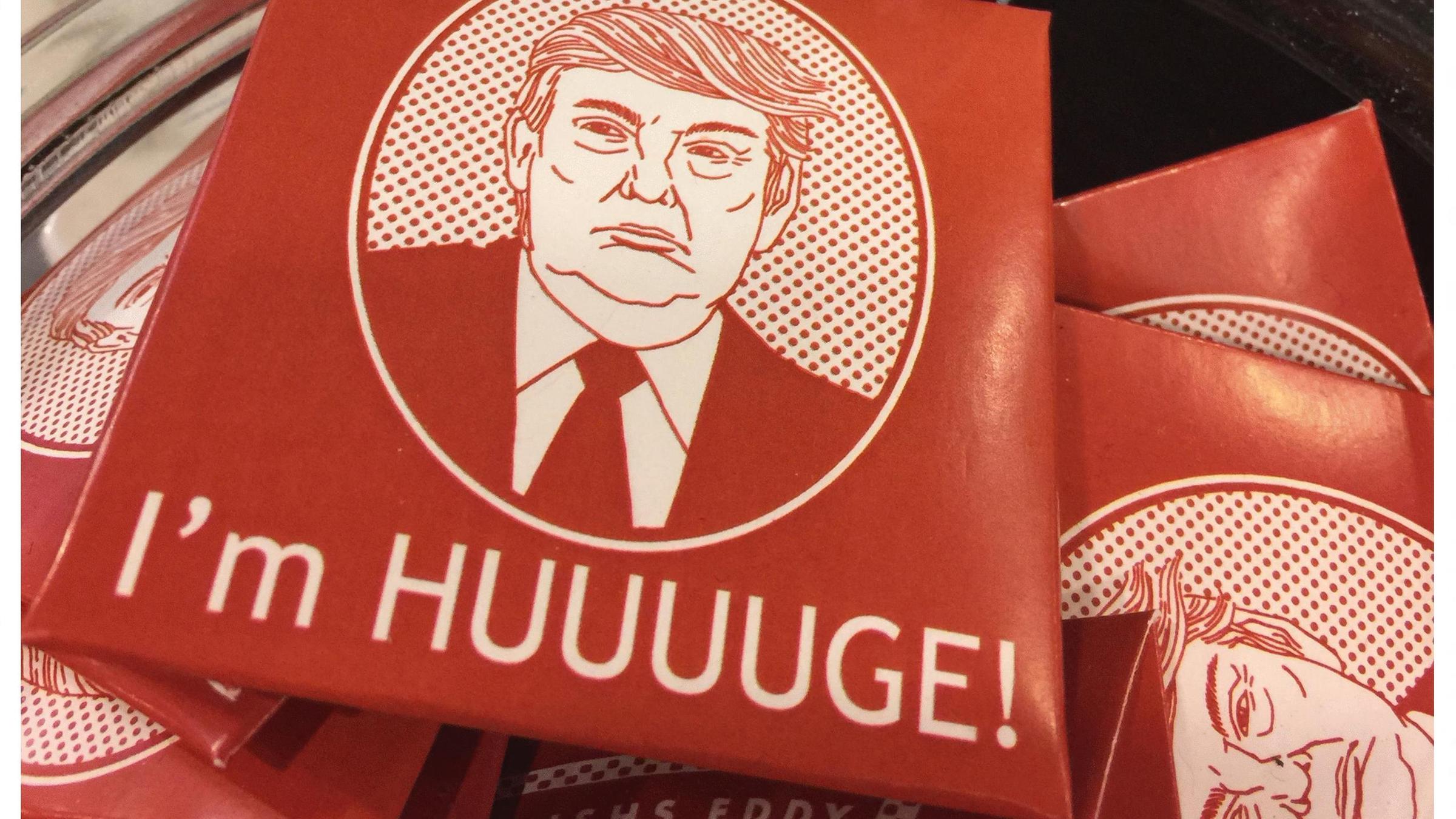 Auf einem Schild steht Trump Condom $4,50 und darunter ist eine Packung mit einer Abbildung von Trump auf der steht "I'm HUUUUGE!" 