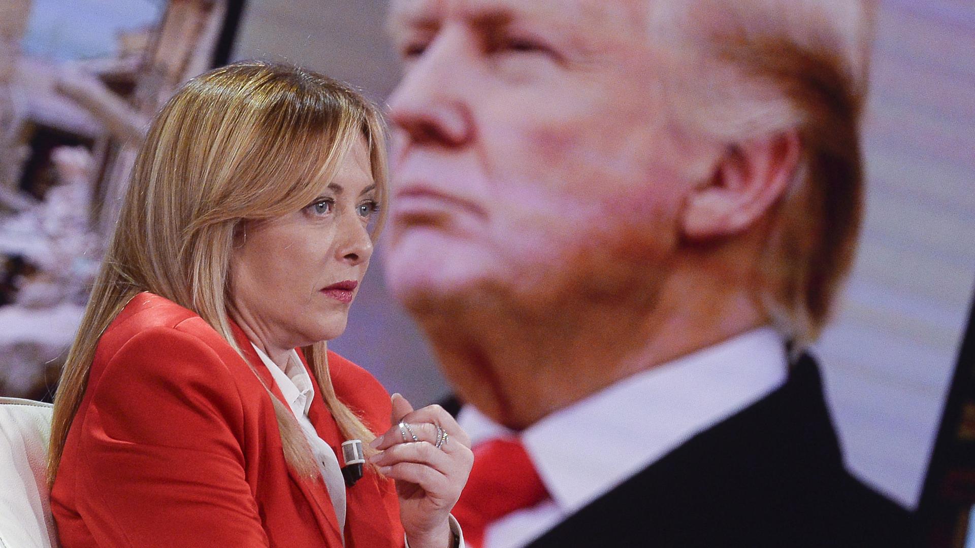 Giorgia Meloni sitzt in einer Talkshow. Im Hintergrund ist das Profil von Donald Trump zu sehen.