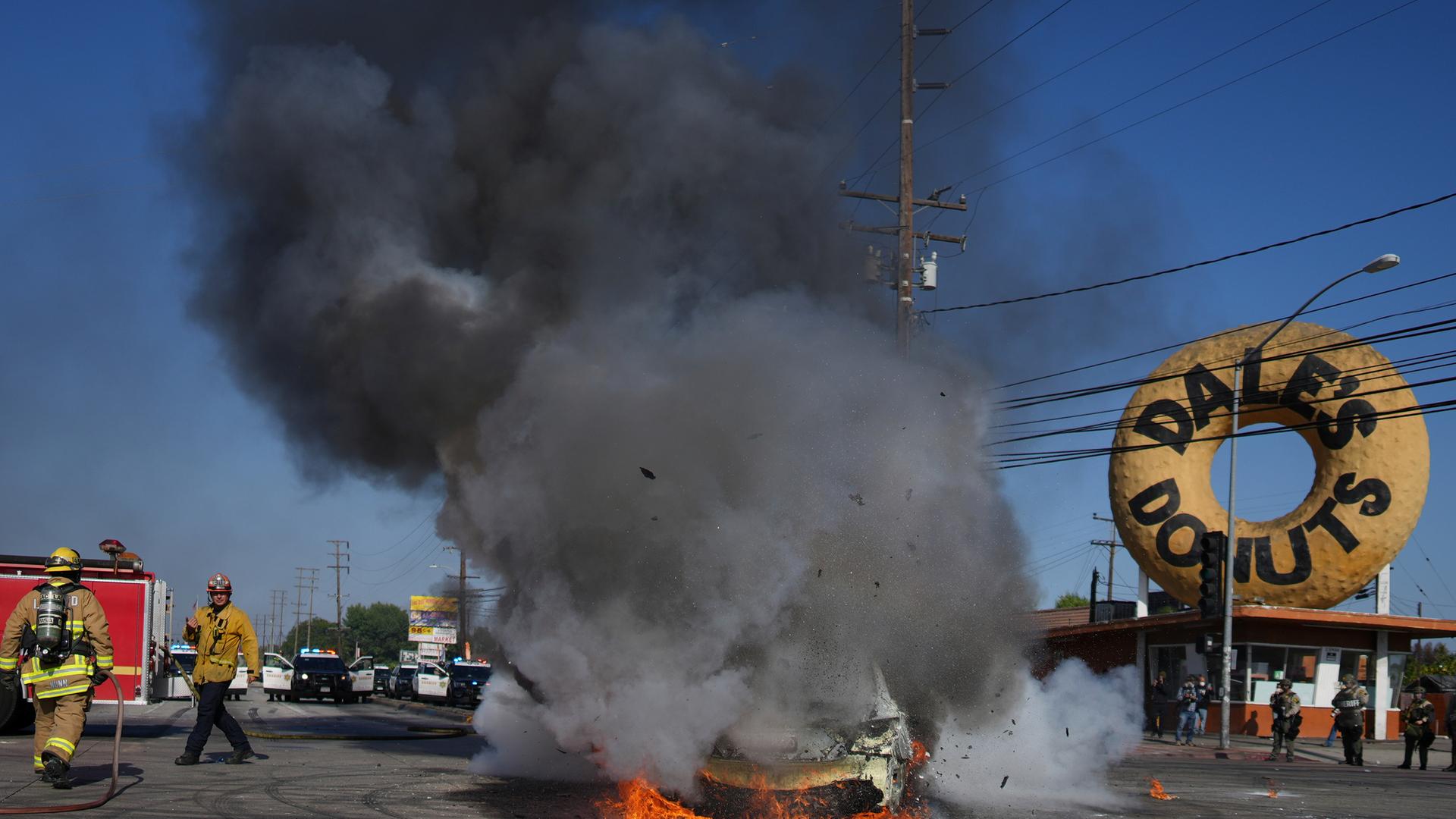 Feuerwehrleute stehen neben einem brennenden Auto während einer Demonstration in Compton, nachdem die Bundeseinwanderungsbehörden Operationen durchgeführt hatten.