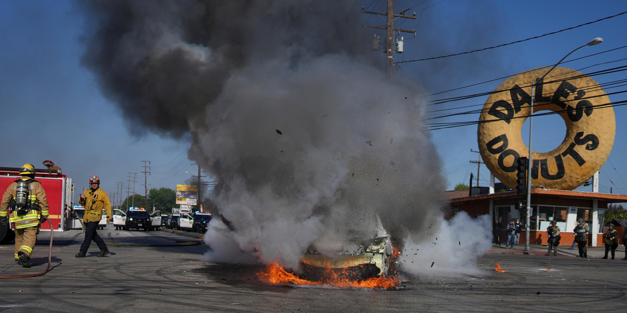 Feuerwehrleute stehen neben einem brennenden Auto während einer Demonstration in Compton, nachdem die Bundeseinwanderungsbehörden Operationen durchgeführt hatten.