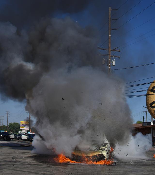 Feuerwehrleute stehen neben einem brennenden Auto während einer Demonstration in Compton, nachdem die Bundeseinwanderungsbehörden Operationen durchgeführt hatten.