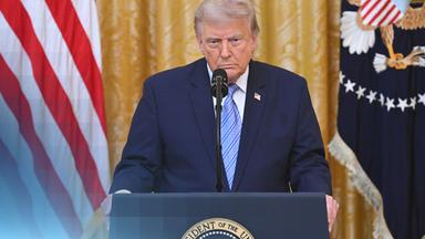 US-Präsident Donald Trump an seinem Rednerpult. Er guckt ernst und trägt einen dunkelblauen Anzug.