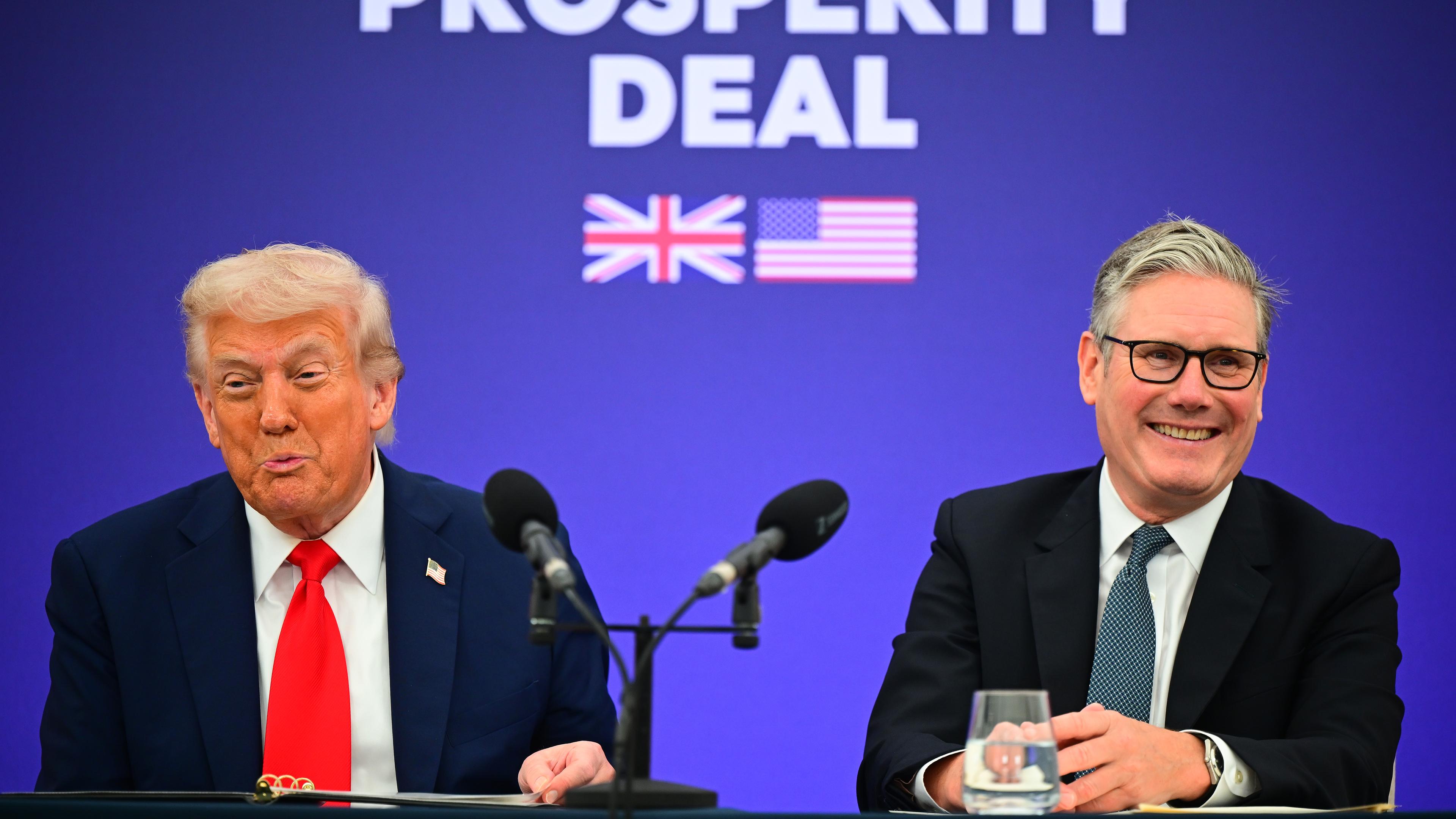 Donald Trump und Keir Starmer vor einer blauen Wand auf der "Prosperity Deal" steht. Starmer lacht.
