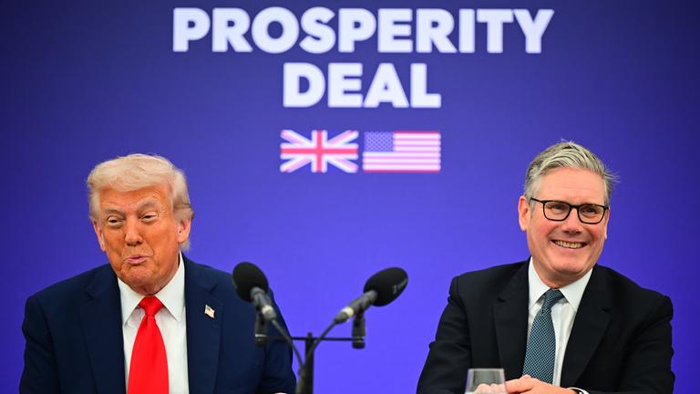 Donald Trump und Keir Starmer vor einer blauen Wand auf der "Prosperity Deal" steht. Starmer lacht.