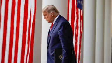 Donald Trump vor USA Flagge schaut nach unten.