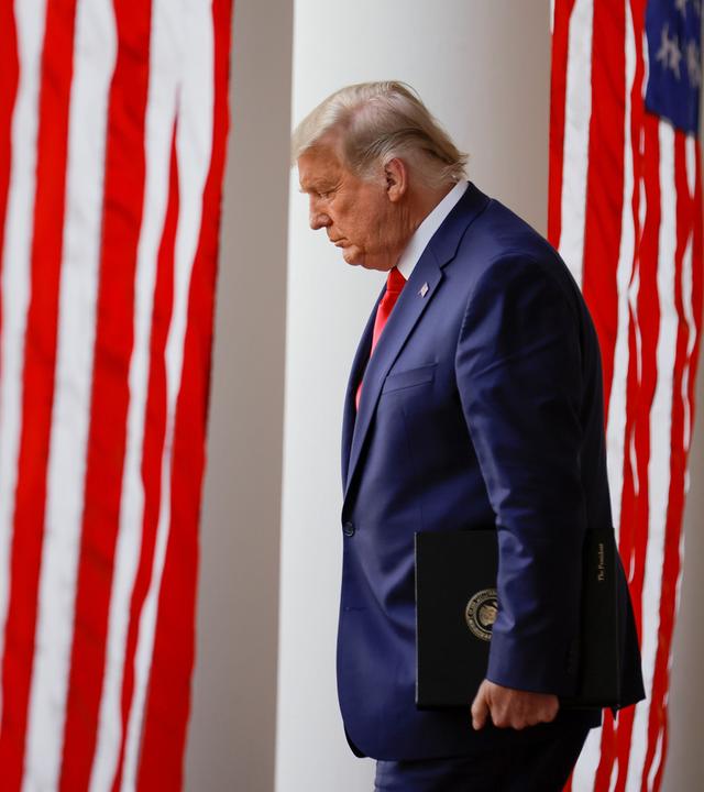 Donald Trump vor USA Flagge schaut nach unten.