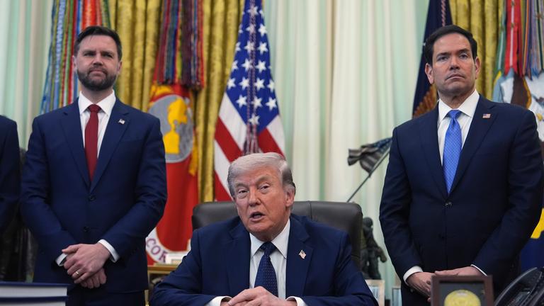 Donald Trump hält eine Rede, während seine Berater Marc Rubio und JD Vance hinter ihm stehen.