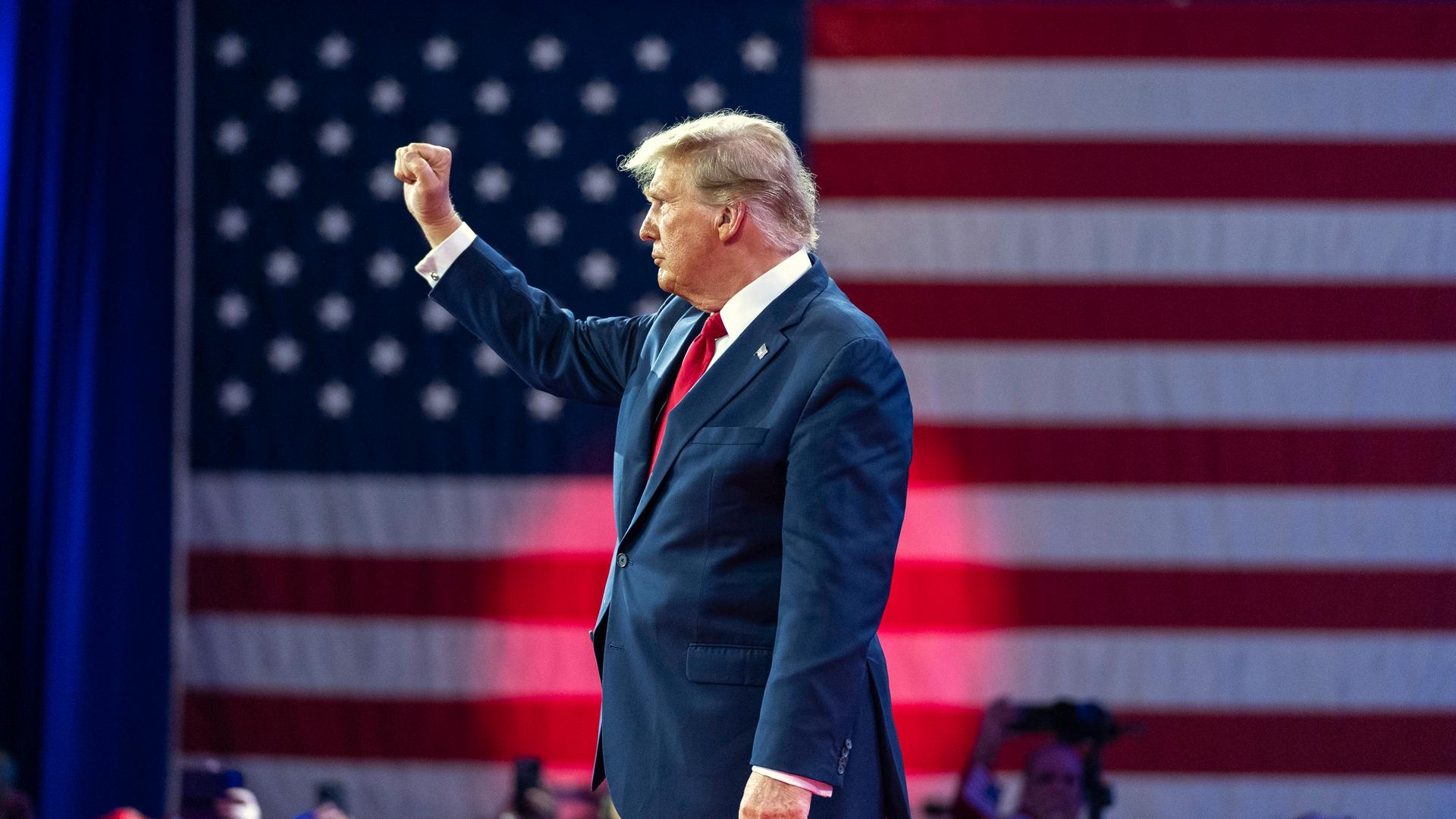 Trump steht vor eine US-Flagge und hebt seine Faust.