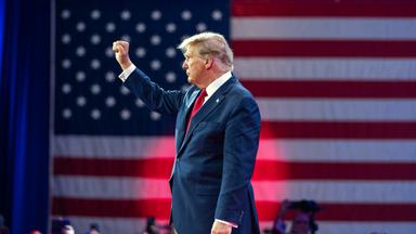 Trump steht vor eine US-Flagge und hebt seine Faust.