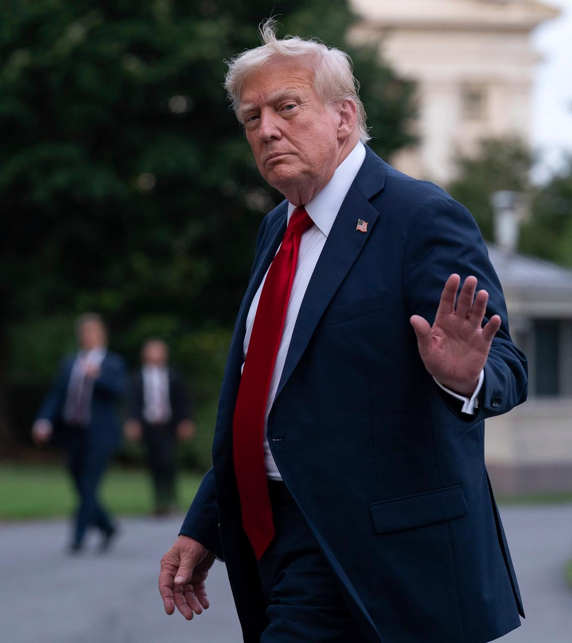 US-Präsident Trump trägt einen dunklen Anzug mit Krawatte und einer Stecknadel mit der Flagge der USA. Er winkt den Reportern.