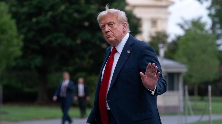 US-Präsident Trump trägt einen dunklen Anzug mit Krawatte und einer Stecknadel mit der Flagge der USA. Er winkt den Reportern.