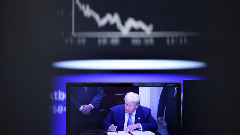 Ein Fernsehbildschirm mit US-Präsident Donald Trump ist am 1. August 2025 an der Börse in Frankfurt am Main zu sehen, im Hintergrund ist der Kursverlauf des deutschen Aktienindex DAX zu erkennen. 