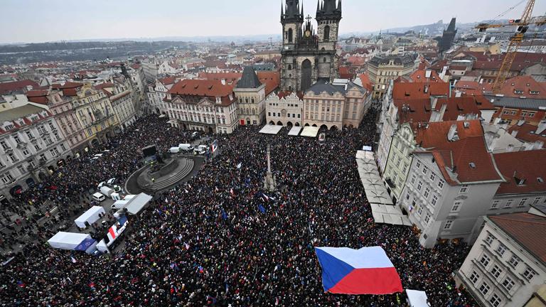 Luftaufnahme einer Menschenmasse aufe einem großen Platz vor einer Kirche, unten rechts ist eine große tschechische Flagge zu sehen.