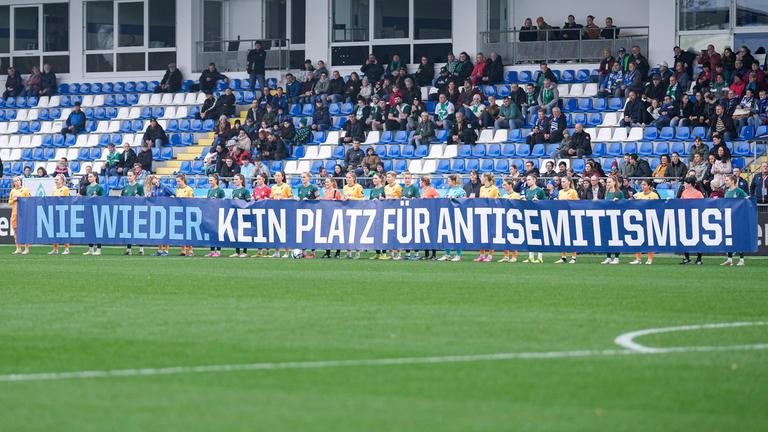 Spielerinnen von TSG 1899 Hoffenheim und SV Werder Bremen mit einem Banner vor dem Anpfiff: Spruchband mit der Aufschrift: Nie wieder. Kein Platz für Antisemitismus