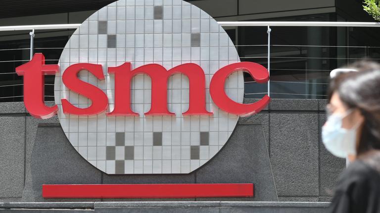 Das Logo der TSMC, am Rand läuft eine Frau mit Maske ins Bild
