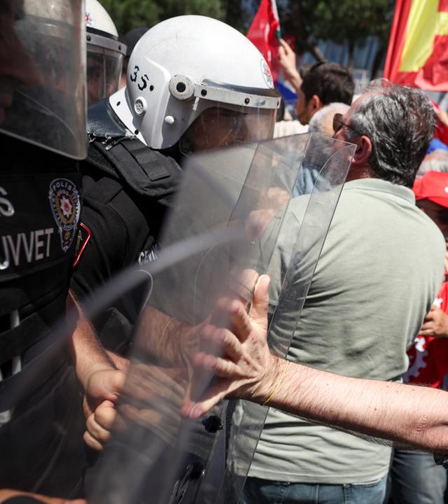 Ein Polizist in Schutzkleidung und Schild und ein Demonstrant mit ausgestrecktem Arm treffen aufeinander.