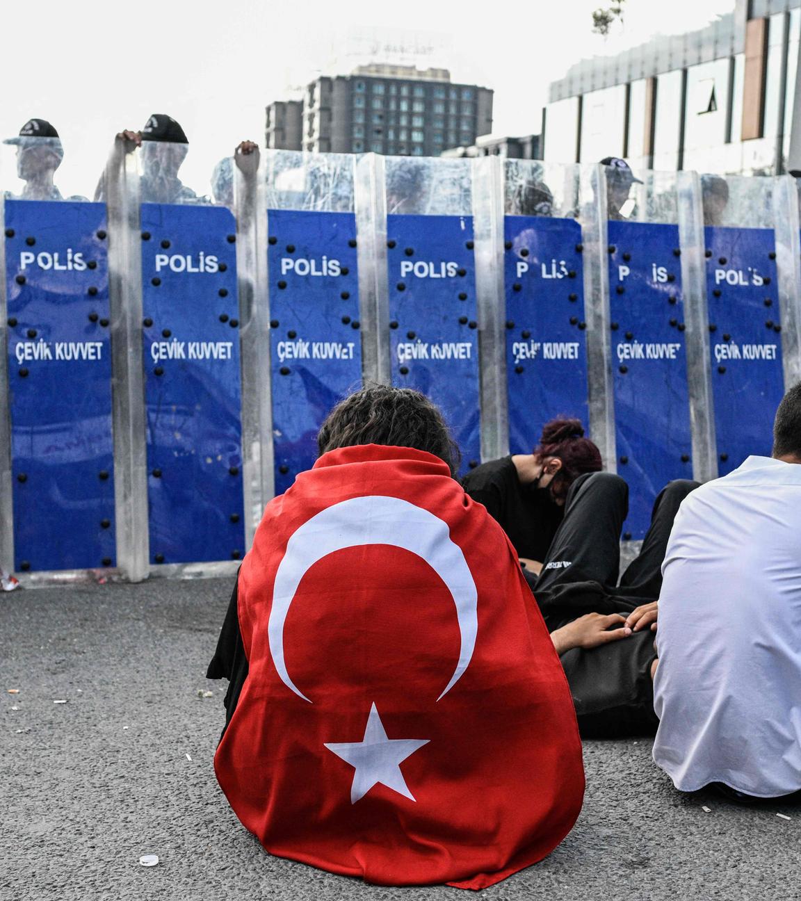 Ein Demonstrant trägt sitzend vor einer Polizeiblockade in Istanbul eine türkische Flagge um den Rücken gebunden.
